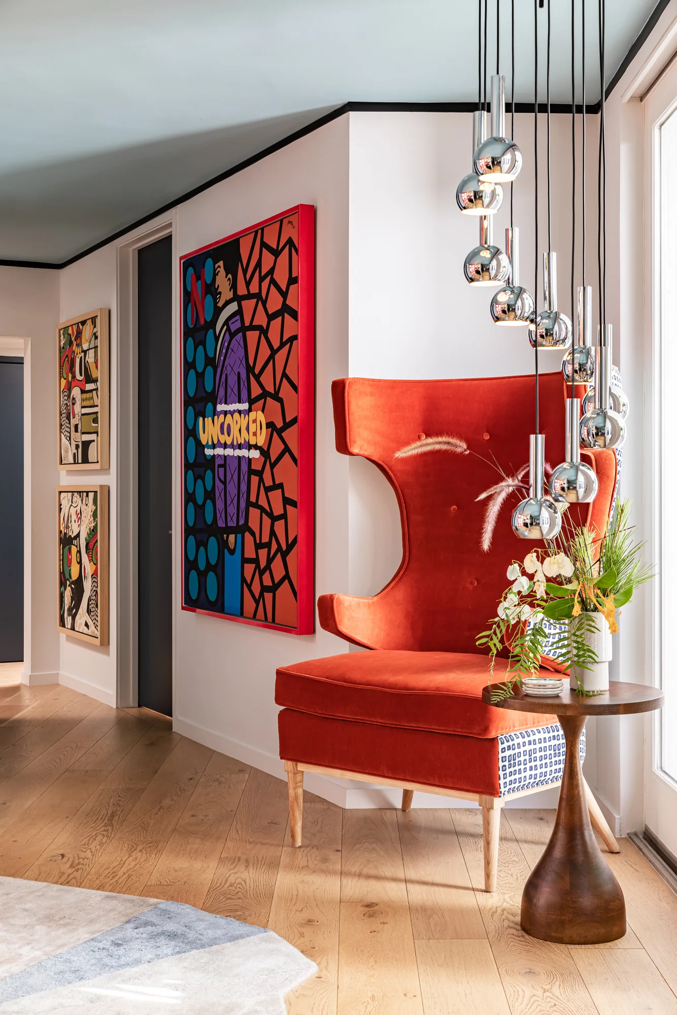 Entry with a cascade of chrome pendants above a red velvet chair