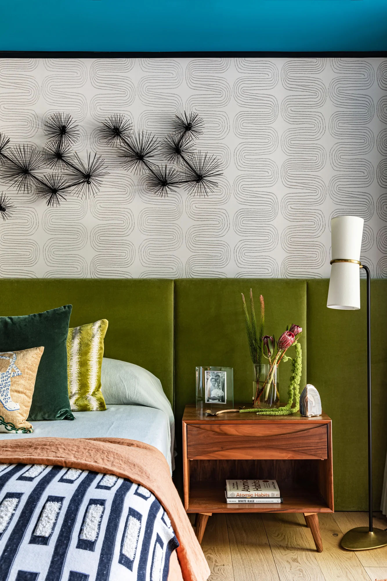 Olive velvet bed against textured wallpaper with a sputnik wall sculpture