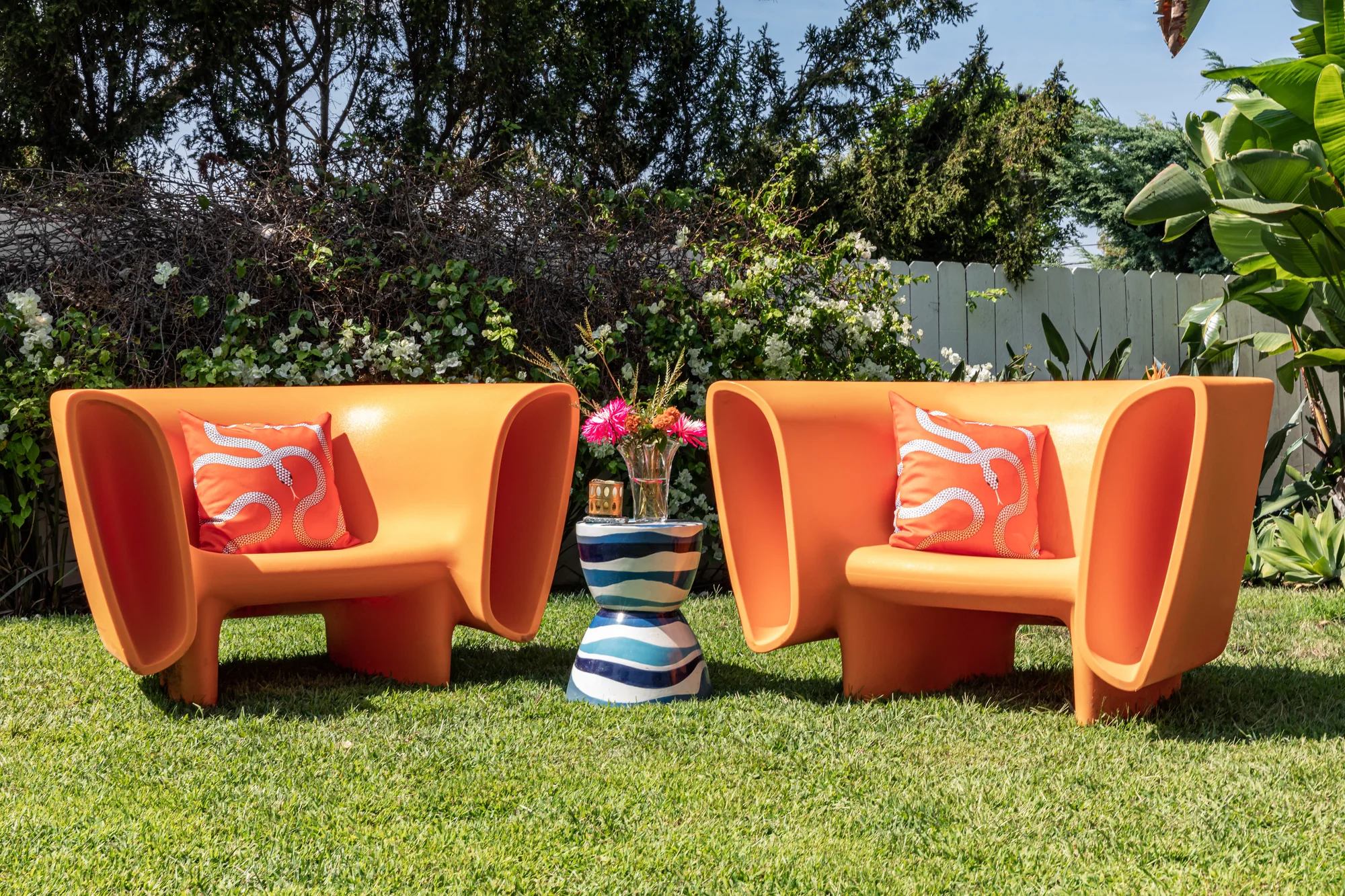 Orange outdoor chairs and a striped side table on the lawn