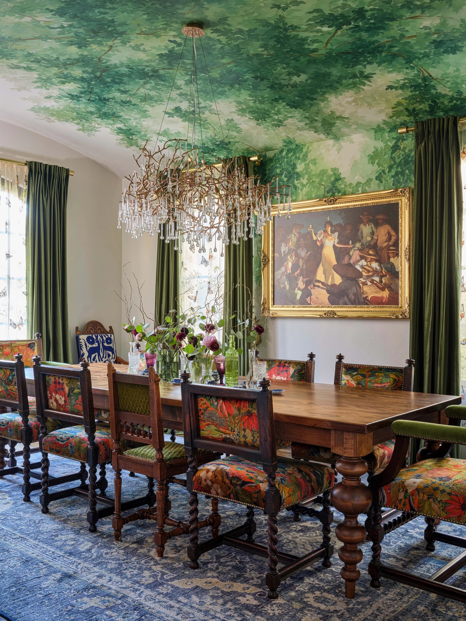 The carved dining table and embroidered chairs beneath the painted-foliage ceiling