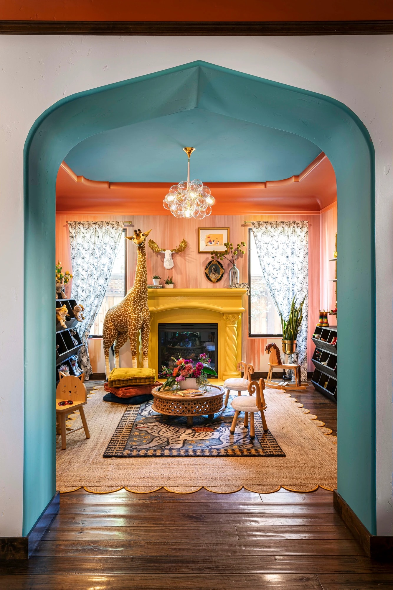 A scalloped teal archway into the coral playroom, a toy giraffe standing by the fireplace