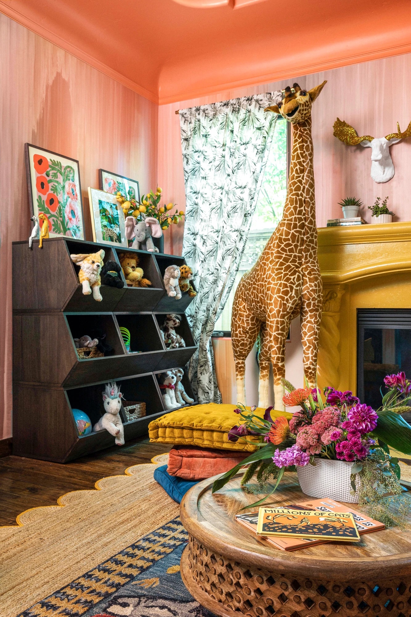 The giraffe standing beside the canary-yellow fireplace, framed by botanical-print curtains