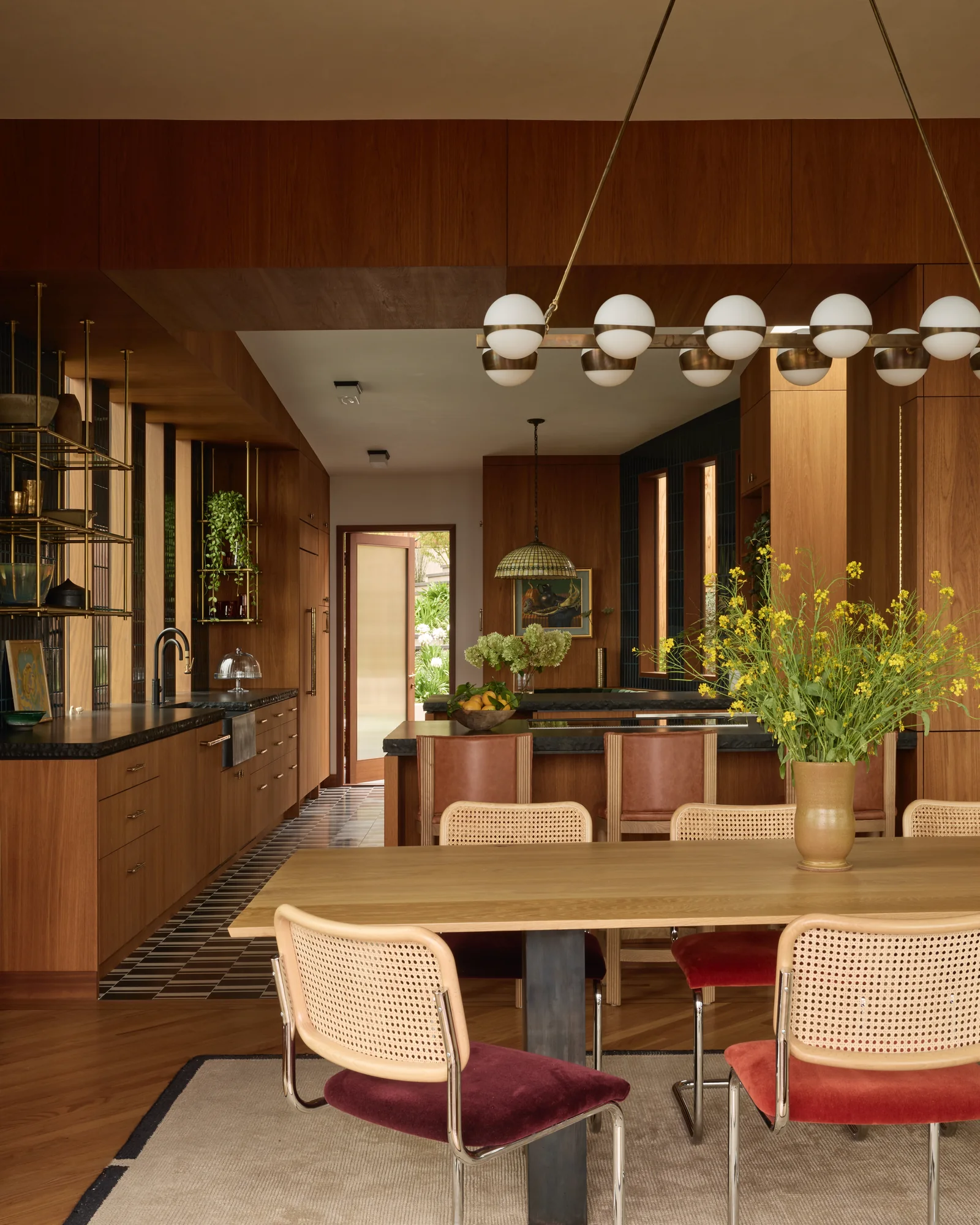 Dining table under a row of globe pendants in the wood-lined kitchen